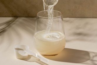 Mięsnisty kulturysta trzymający słoik z białym proszkiem kreatyny obok hantli w siłowni