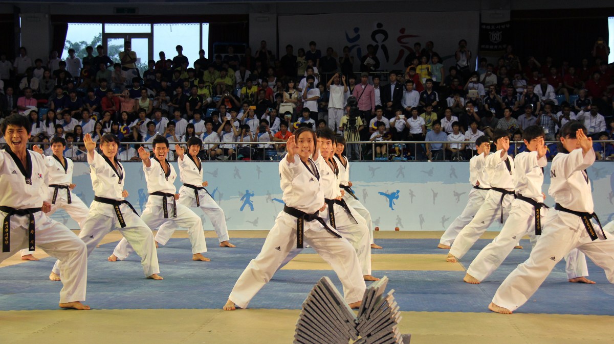 Fighter w ochraniaczach wykonuje wysokie kopnięcie roundhouse na poduszce