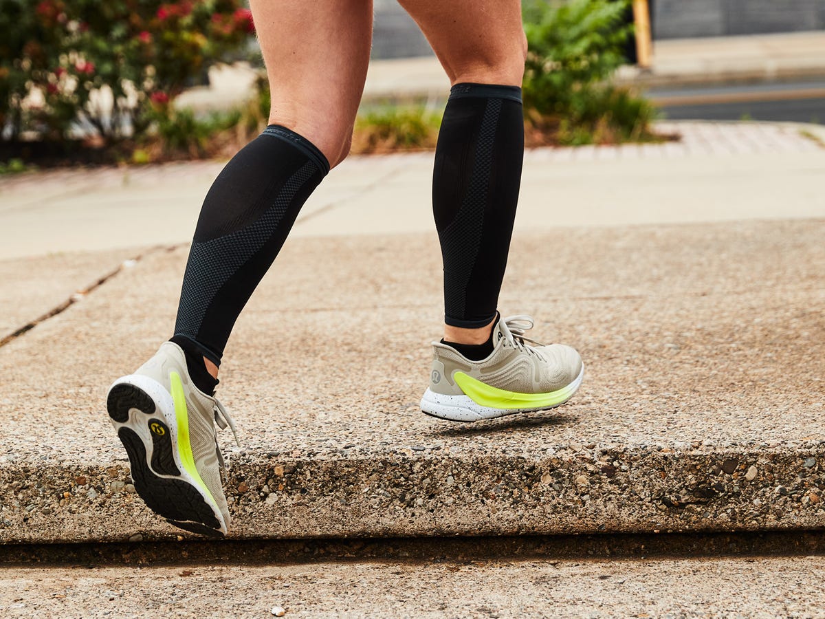 Kobieta zakłada czarne skarpety kompresyjne na obolałe łydki po treningu