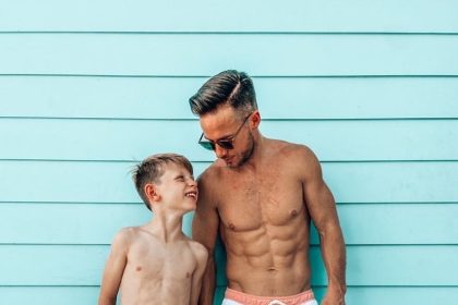 mężczyzna w granatowych szortach kąpielowych stoi przy krawędzi basenu z turkusową wodą