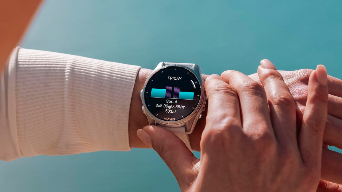 Garmin Fenix 7 i Apple Watch Ultra obok siebie na drewnianym stole z linijką