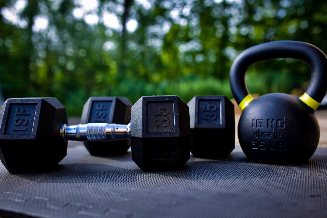 Cena i wszechstronność sprzętu treningowego kettlebell i hantle ułożone obok siebie na macie